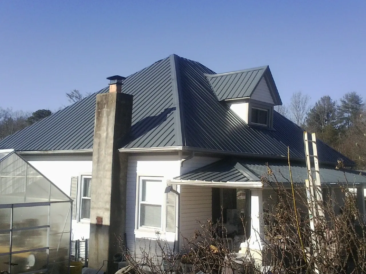 Dark blue standing seam metal roof on a white farmhouse with dormer — Slate & Tile Roof Repair by Roofing Brothers in Magna