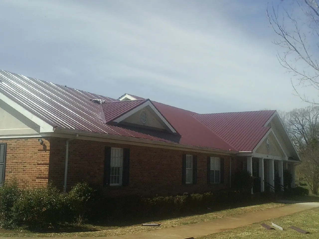 Red metal roof with gabled entries on a long brick building, from a Hail Damage Roof Repair job in Magna