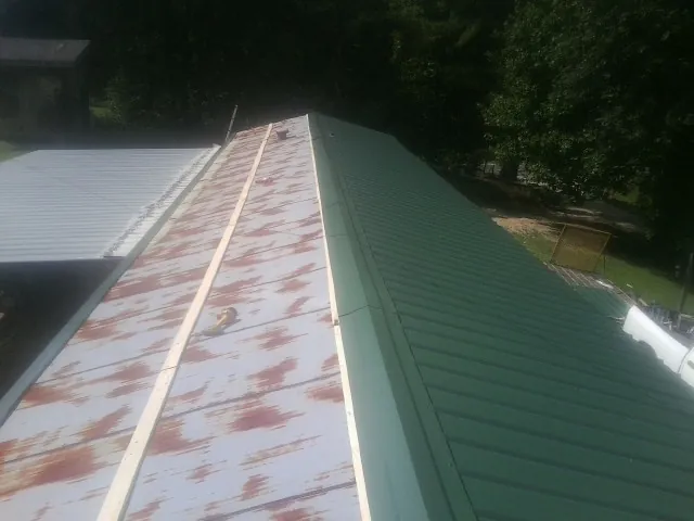 Old rusted panels beside newly installed green metal roofing — Wind Damage Roof Repair by Roofing Brothers in Magna