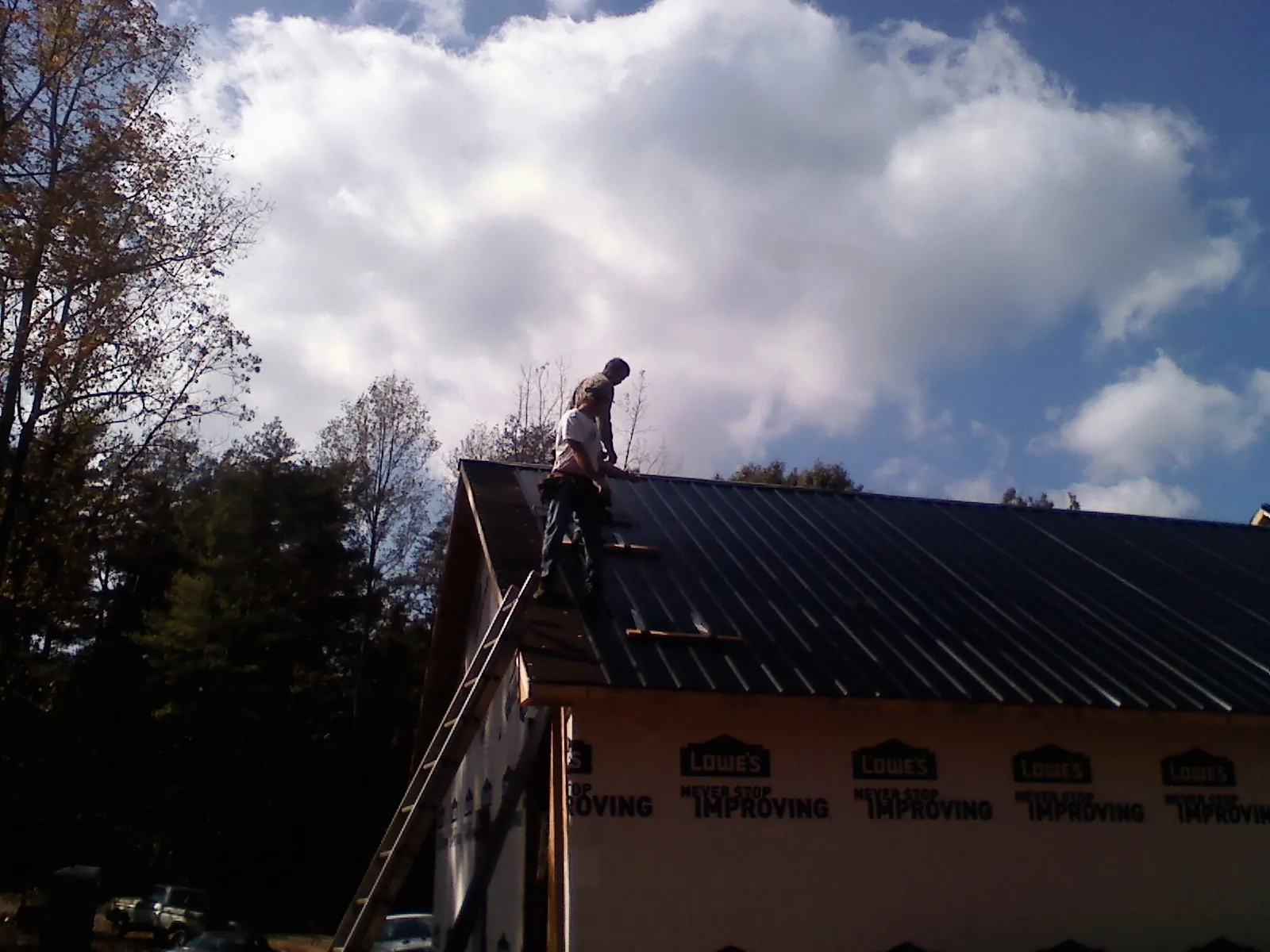 Roofer fastening dark metal panels high against a cloudy sky, from a Roof Inspection job in Magna