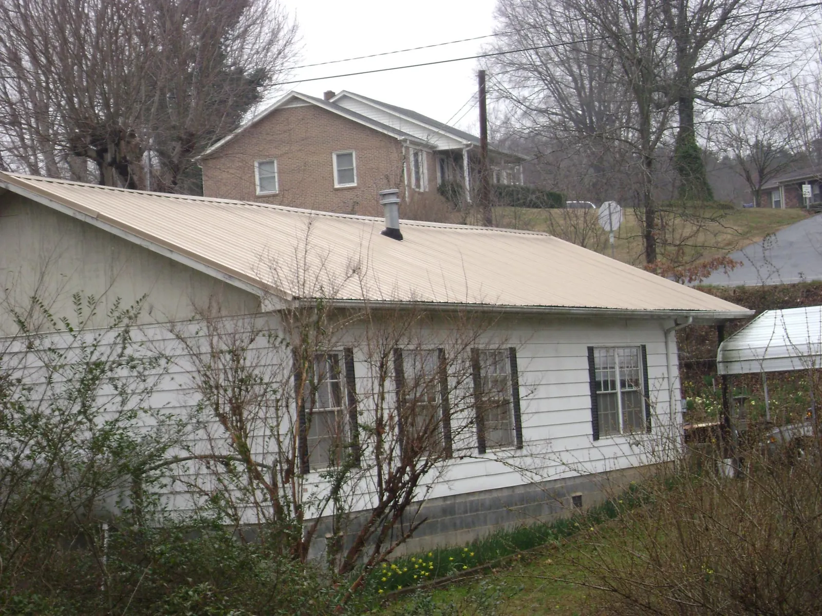 Tan metal roof on a white sided house set into a hillside — Commercial Roofing by Roofing Brothers in Magna